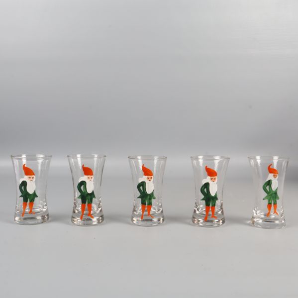 Fem snapsglas med tomtemotiv i rad mot ljus bakgrund