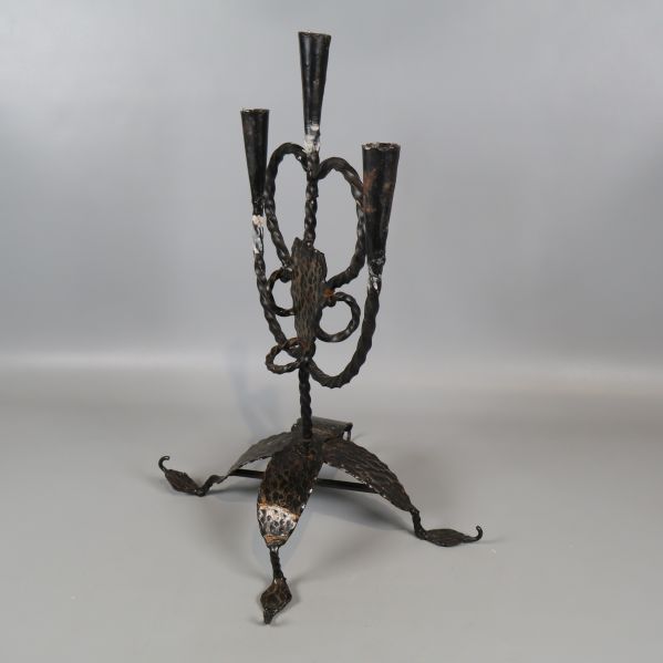 Smidesljusstake sedd snett bakifrån mot grå bakgrund