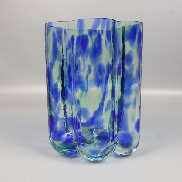 Vas i glas med böljande form och blågröna toner, sedd snett bakifrån