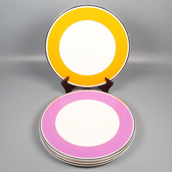 Fyra mattallrikar med orange och lila kant på ställ