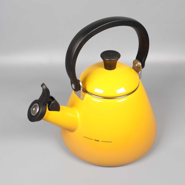 Gul vattenkittel med svart handtag och vissla fotograferad snett framifrån