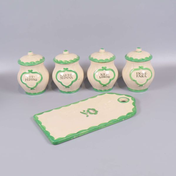 Fyra kryddburkar och en rektangulär skärbräda med grön kant