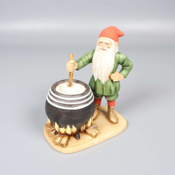 Tomte med vit skägg rör om i stor svart gryta