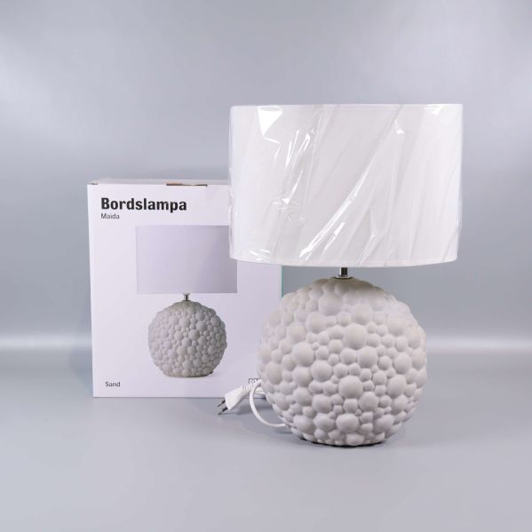 Vit bordslampa med bubblig bas framför originalförpackning