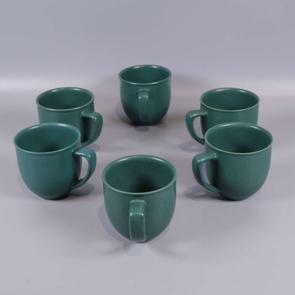Sex gröna kaffekoppar uppställda i cirkel på bord