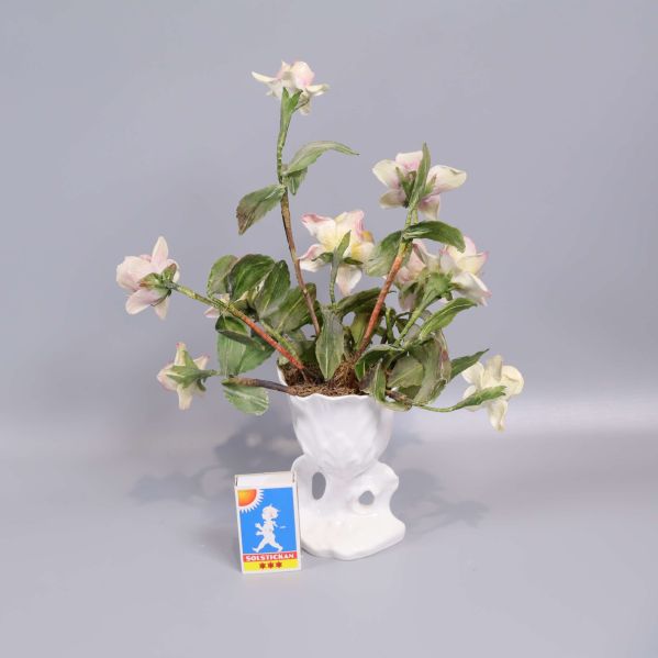 Vas med konstblommor bredvid tändsticksask för storleksjämförelse