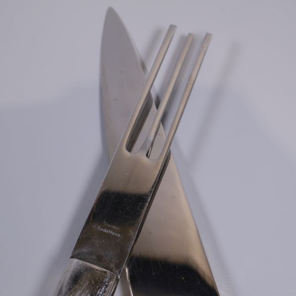 Närbild på tranchersetets gaffel och kniv, präglad logga synlig