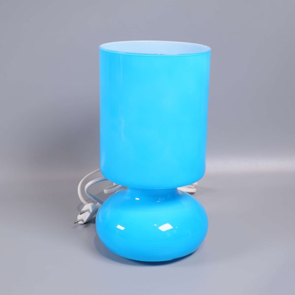 Blå cylinderformad bordslampa med vit sladd mot grå bakgrund