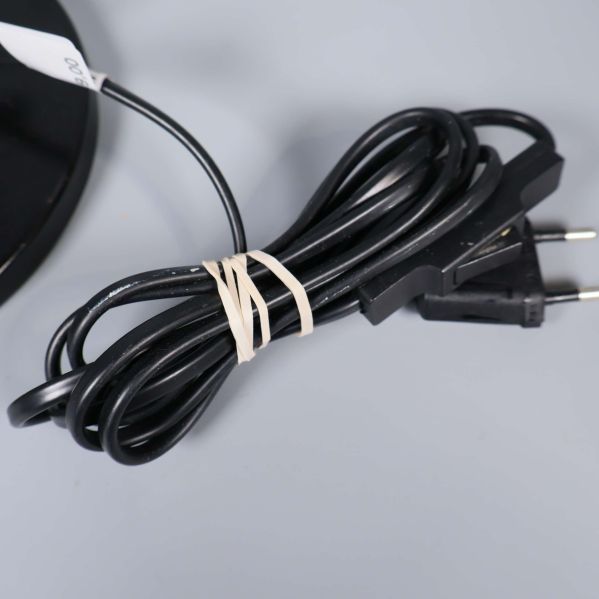 Svart elkabel med kontakt hoprullad vid lampfoten