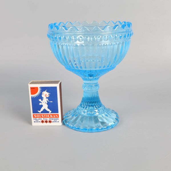 Ljusblå glasskål jämte en tändsticksask för storleksreferens