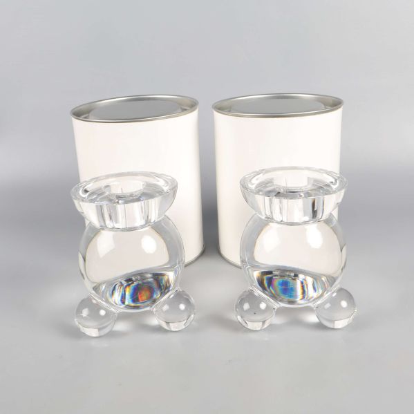 Två runda glasljusstakar framför vita cylindriska förpackningar