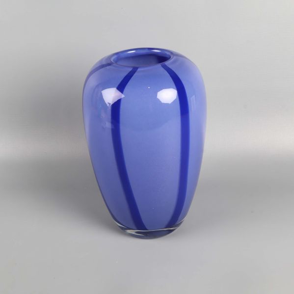 Blå glasvas med mörka ränder fotograferad mot grå bakgrund