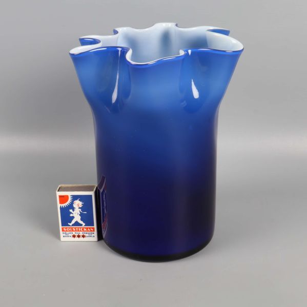 Blå vågig vas jämte tändsticksask för storleksreferens