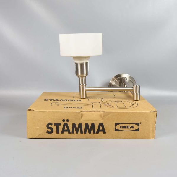 Vägglampa med vit skärm och metallarm står på STÄMMA-låda