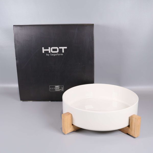 Vit serveringsskål i träställning med svart förpackning i bakgrunden