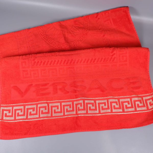 Utbredd röd handduk med VERSACE-logga och grekisk bård