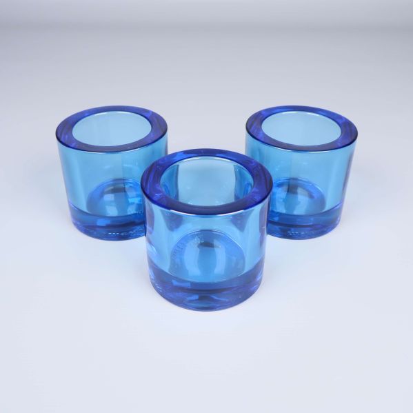 Tre ljuslyktor i blått glas uppställda i en triangel på vit bakgrund