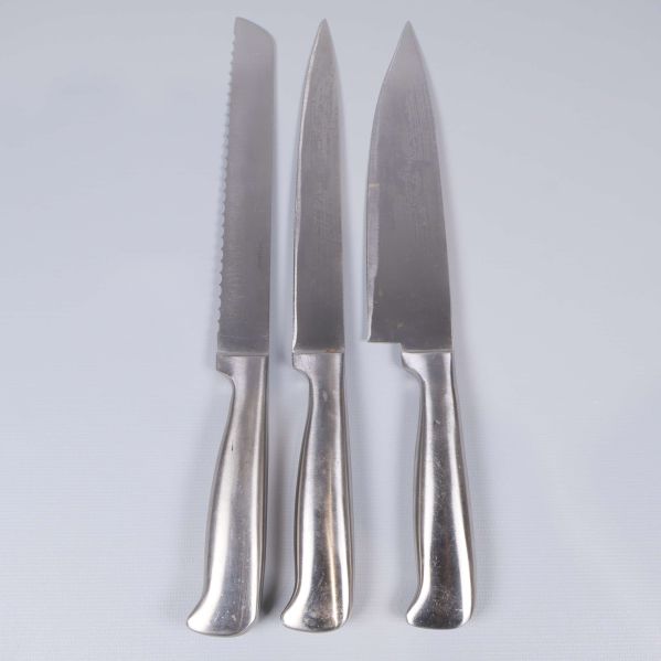 Tre blanka köksknivar med olika blad på ljus bakgrund