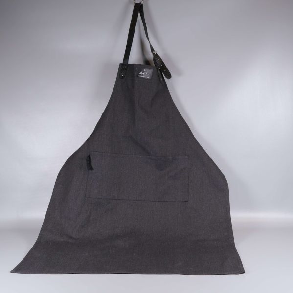 Helt förkläde i mörkt tyg hänger mot vit bakgrund