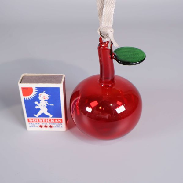 Ett rött glasäpple bredvid tändsticksask för storleksjämförelse