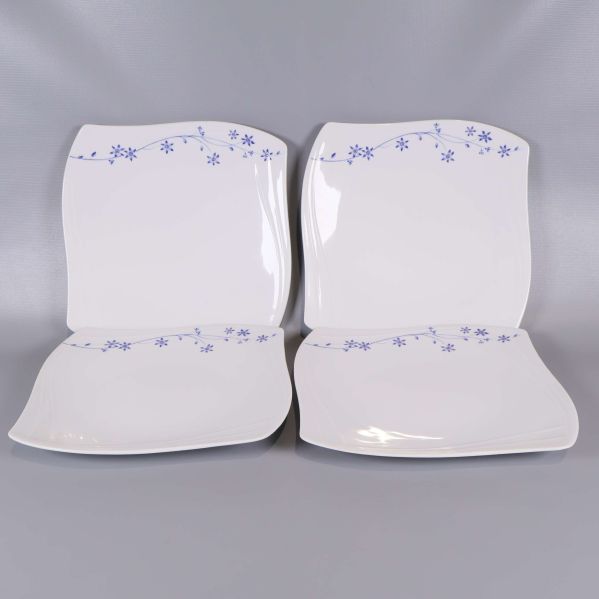 Fyra vita fyrkantiga tallrikar med blå blommönster längs kanten