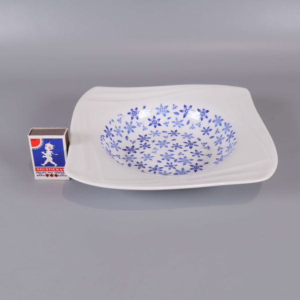 En djup tallrik med blå blommor bredvid tändsticksask