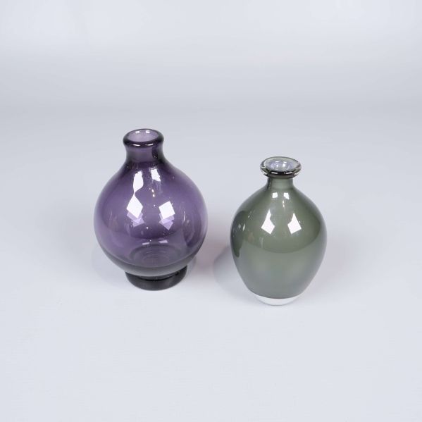 Två runda glasvaser, en lila och en grågrön, står sida vid sida