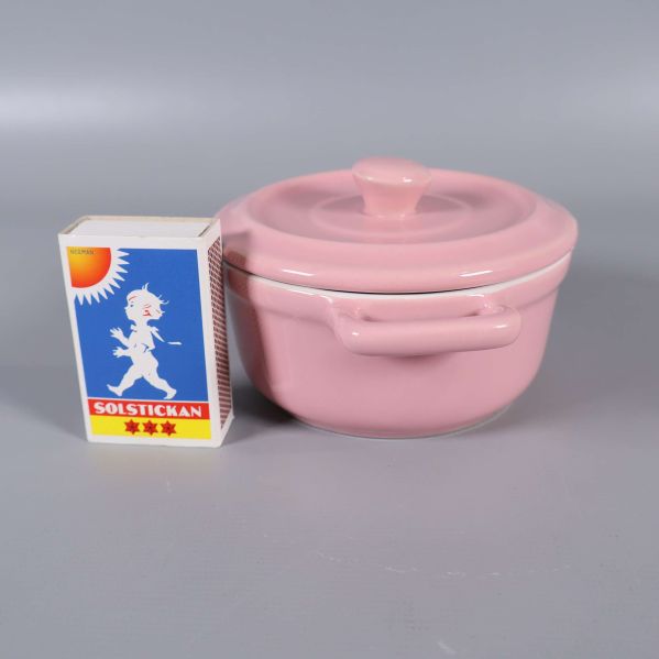 Rosa minigryta med lock bredvid en tändsticksask