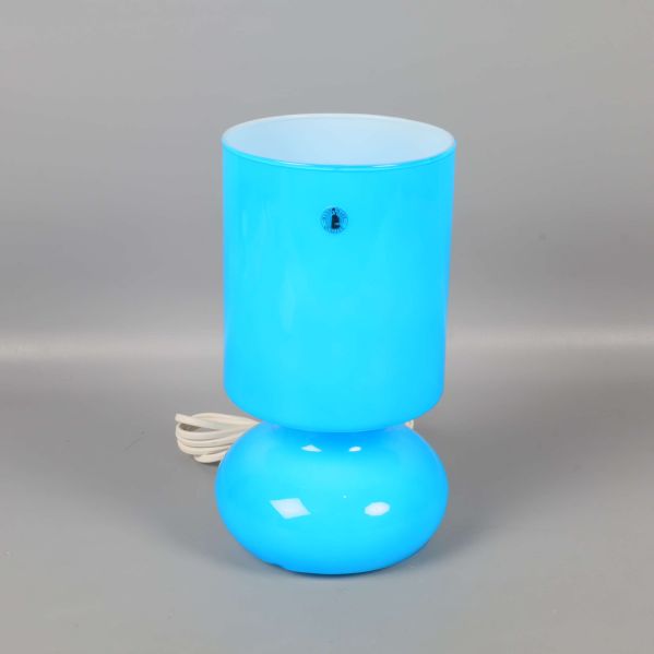 Blå cylinderformad bordslampa med rund fot mot grå bakgrund