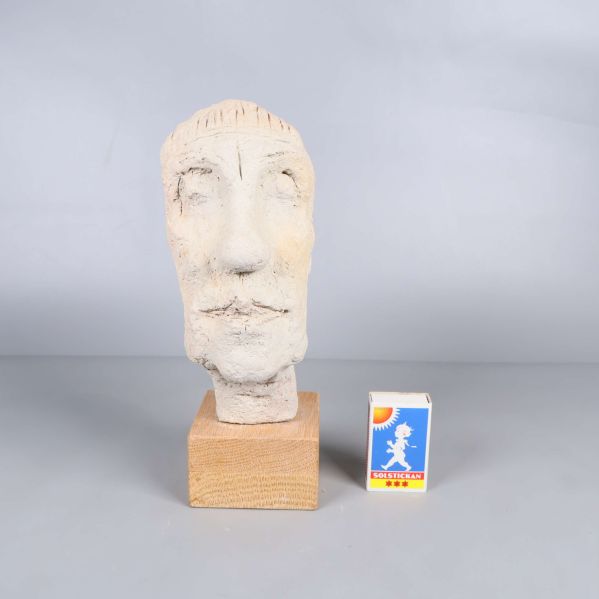 Skulpturhuvud på träbas bredvid tändsticksask