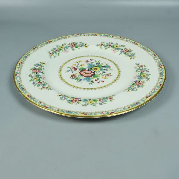 Tallrik med blommigt mönster och guldkant liggande på bord