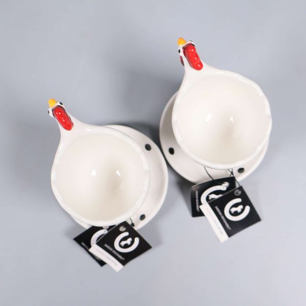 Två vita ägghållare med hönshuvud och svarta prickar