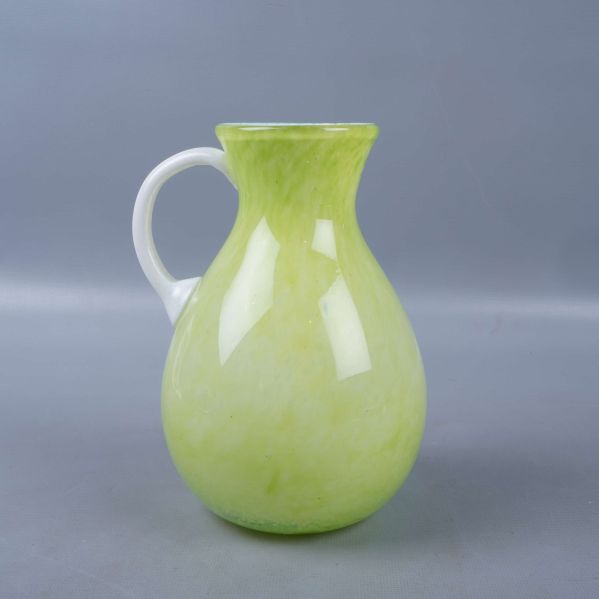 Vas i grönt glas med vitt handtag sedd från sidan