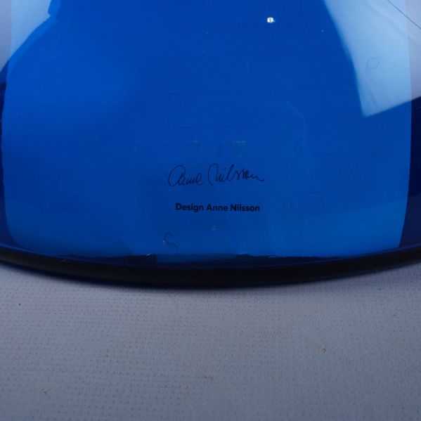 Närbild av signatur och designtext på blå glasvas