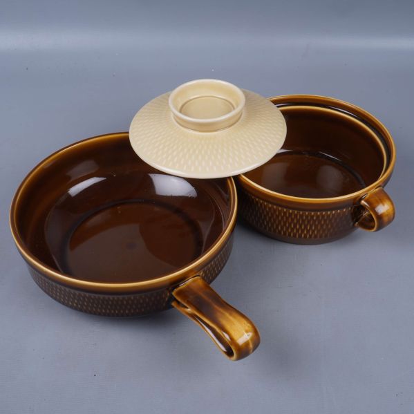 Två bruna serveringsskålar med handtag och lock i ljust mönster