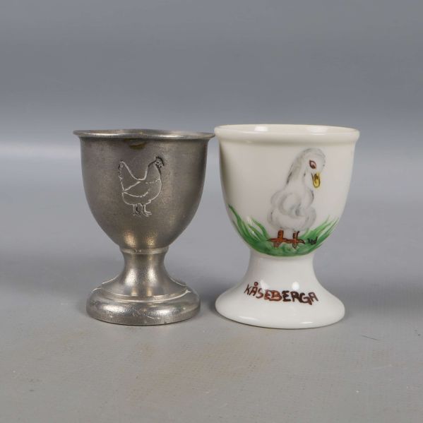 Två ägghållare, en metall en keramik med kycklingmotiv