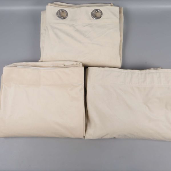 Tre vikta beige gardinlängder på grå bakgrund