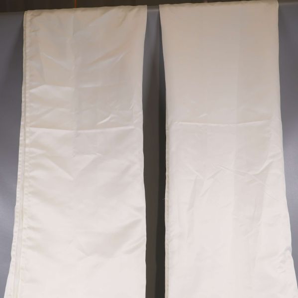 Två vita gardinlängder hänger mot grå bakgrund