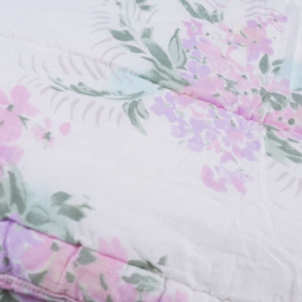 Närbild av täcke med rosa och lila blommor samt gröna blad