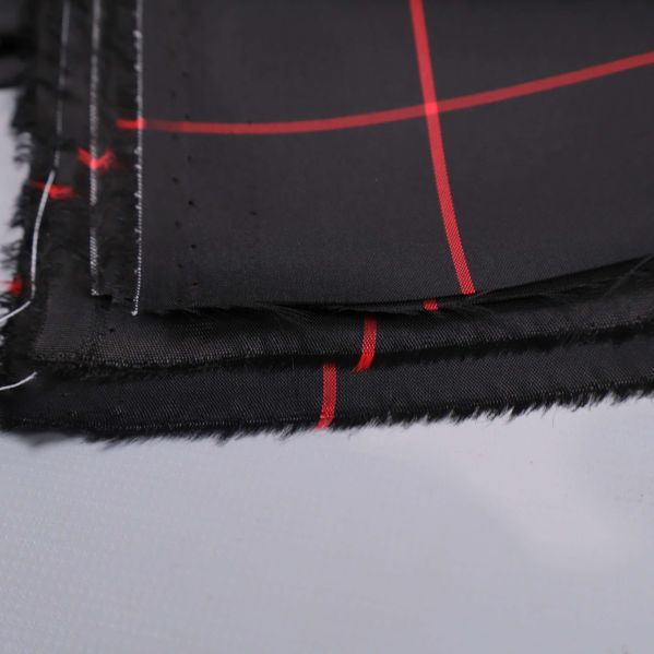 Närbild av rå kant på svart tyg med röda rutor