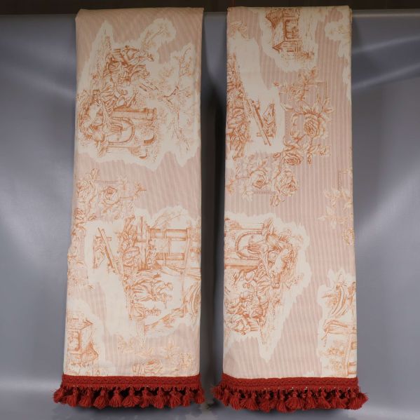 Två vikta gardinlängder med tofsar mot grå bakgrund