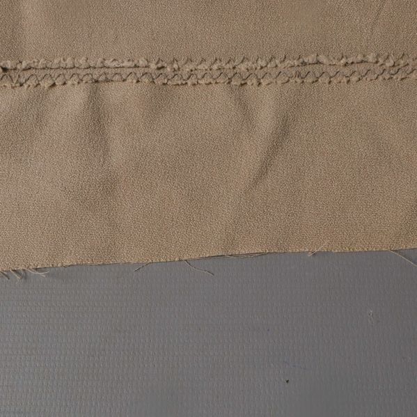 Närbild på beige tygs struktur med söm i övre delen