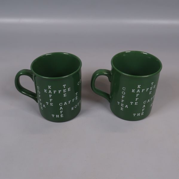 Två gröna kaffekoppar med vit text från sidan