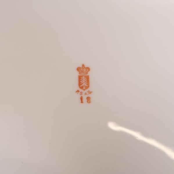 Närbild på porslinsstämpel med röd dekor och krona
