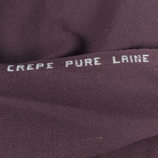 Texten CREPE PURE LAINE tryckt på lila tyg