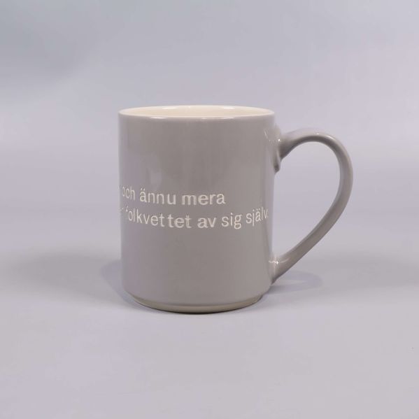 Grå mugg med vitt citat och handtag till höger