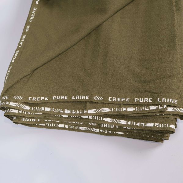 Olivgrönt tyg, kanten visar texten Crepe Pure Laine
