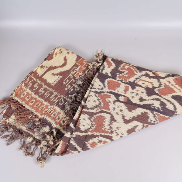 Textil med mönster och fransar delvis vikt på ljus bakgrund