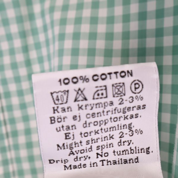 Materiallapp med text 100% bomull och skötselråd på rutig skjorta