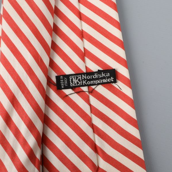 Etikett med Nordiska Kompaniet på röd och beige slips